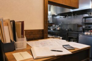 飲食店の事務スペースに置かれたシフト表、給与台帳、電卓、ペン